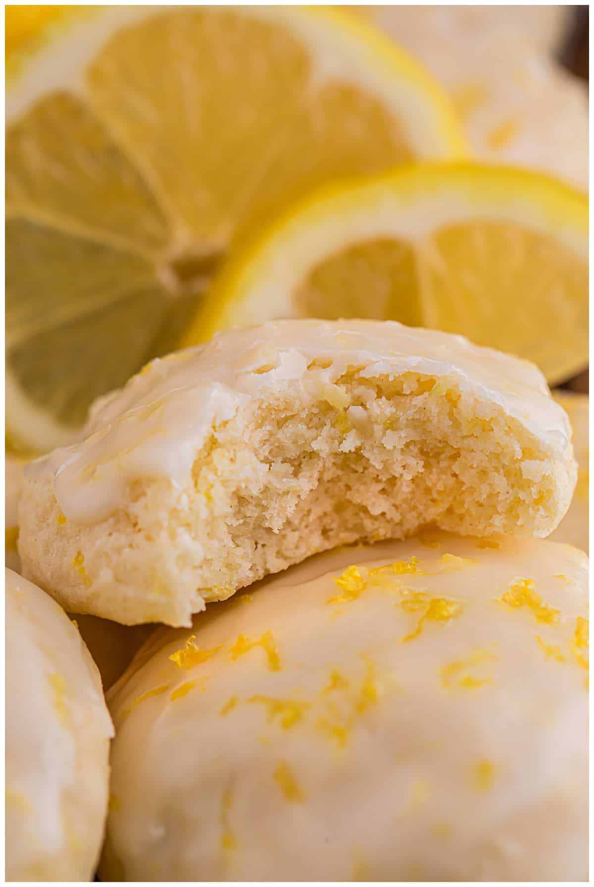 Soft lemon ricotta cookie with a bite taken out, surrounded by fresh lemon slices