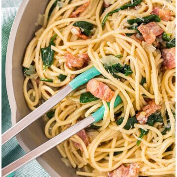 Close-up of bacon and spinach pasta being mixed in the skillet with tongs.