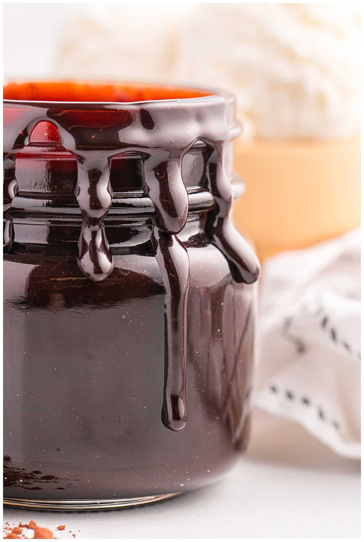 Glass jar of hot fudge sauce with thick drips running down the side.