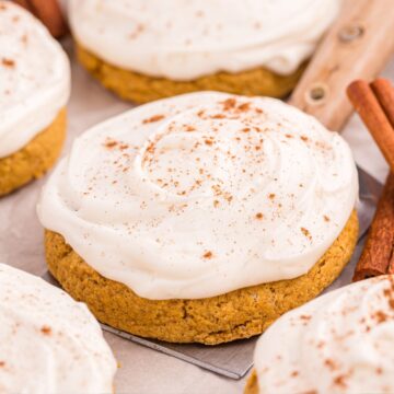 Close up of a soft pumpkin sugar cookie topped with cream cheese frosting and cinnamon sprinkle