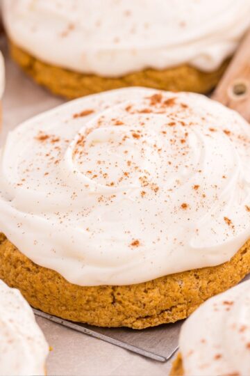 Close up of a soft pumpkin sugar cookie topped with cream cheese frosting and cinnamon sprinkle